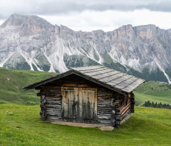 iew of a traditional mountain hut in Dolomites Alps pasture close to Val Gardena and Casterotto, Italy