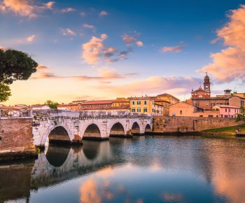Rimini cityscape. Tiberius bridge famous sightseeing in Rimini at dawn. Summer sunrise in Rimini historic center.