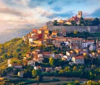 Antique city Motovun Croatia Istria. Picturesque panorama age-old village at hill with pink cloud and sunny light and authentic home with red tegular roof and green vineyard garden.