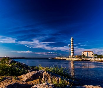 View at the lighthouse in the bay with beach on the other side and beautiful blue sky. Sunrise time. Jesolo, Italy.